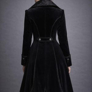 May include: A long, black velvet coat with a high collar and decorative buttons. The coat features intricate trim along the seams and cuffs, and a flared skirt. The back view showcases the coat's tailored design and elegant silhouette.