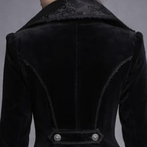 May include: A black velvet jacket with a high collar and decorative buttons. The jacket features intricate stitching along the seams and a detailed pattern on the collar. The sleeves are long and fitted.