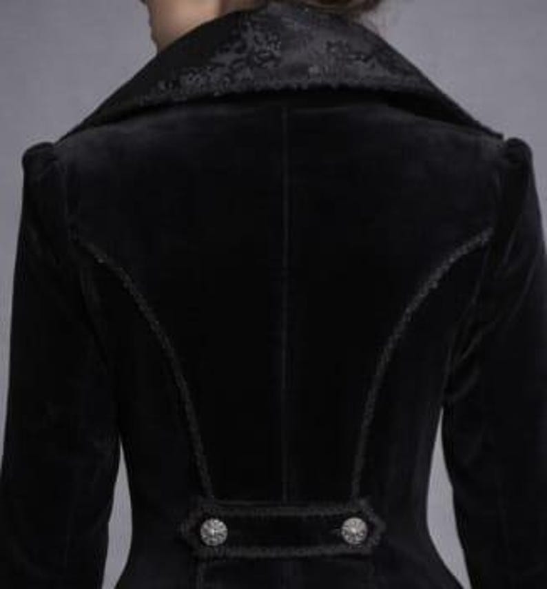 May include: A black velvet jacket with a high collar and decorative buttons. The jacket features intricate stitching along the seams and a detailed pattern on the collar. The sleeves are long and fitted.