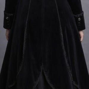 May include: A long, black velvet coat with a flared skirt and intricate lace trim. The coat features decorative buttons on the cuffs and bodice, and a high collar. The overall design suggests a gothic or Victorian aesthetic.