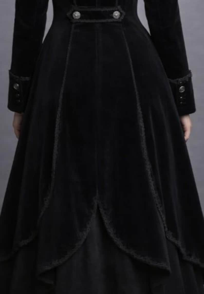 May include: A long, black velvet coat with a flared skirt and intricate lace trim. The coat features decorative buttons on the cuffs and bodice, and a high collar. The overall design suggests a gothic or Victorian aesthetic.