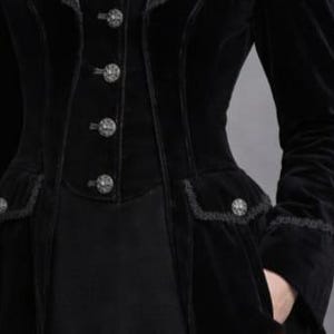 May include: Black velvet coat with decorative buttons and lace trim. The coat features a fitted waist, pockets, and long sleeves. The buttons are ornate and the overall style is gothic.