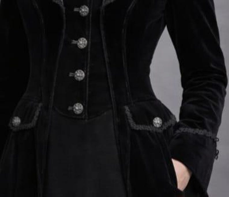 May include: Black velvet coat with decorative buttons and lace trim. The coat features a fitted waist, pockets, and long sleeves. The buttons are ornate and the overall style is gothic.