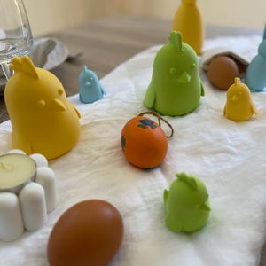 Peut inclure: Une nappe blanche avec une variété de décorations de Pâques, dont un poussin jaune, un poussin vert, un poussin bleu, un œuf brun, un œuf orange et un lapin jaune.