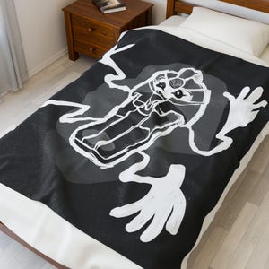 Può includere: Coperta a fantasia in bianco e nero con un'illustrazione stilizzata di una creatura. Il design presenta un corpo lungo e mani tese su uno sfondo scuro con sfumature di grigio.