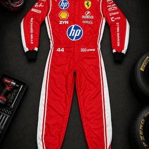 Op de afbeelding: Een rood-wit racepak met het Ferrari-logo, HP-branding en diverse sponsorpatches. Het pak toont het nummer 44 en de naam LEWIS met een Britse vlag. Het is voorzien van lange mouwen met zwarte boorden en een hoge witte kraag.