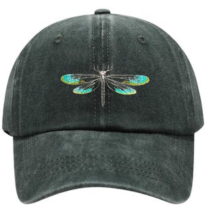 May include: A dark gray baseball cap featuring an embroidered dragonfly design. The dragonfly has teal and yellow wings and a silver body. The cap is made of a soft, textured fabric and has a curved brim.