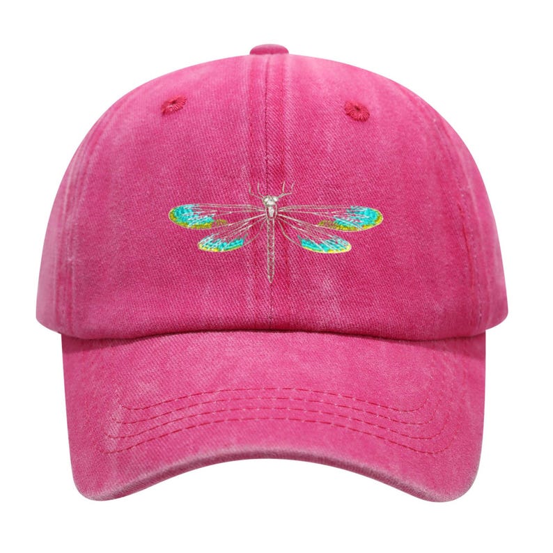 May include: A magenta baseball cap with a curved brim. The cap features an embroidered dragonfly design with silver, teal, and yellow accents. The cap is made of a soft, textured fabric and has an adjustable strap.