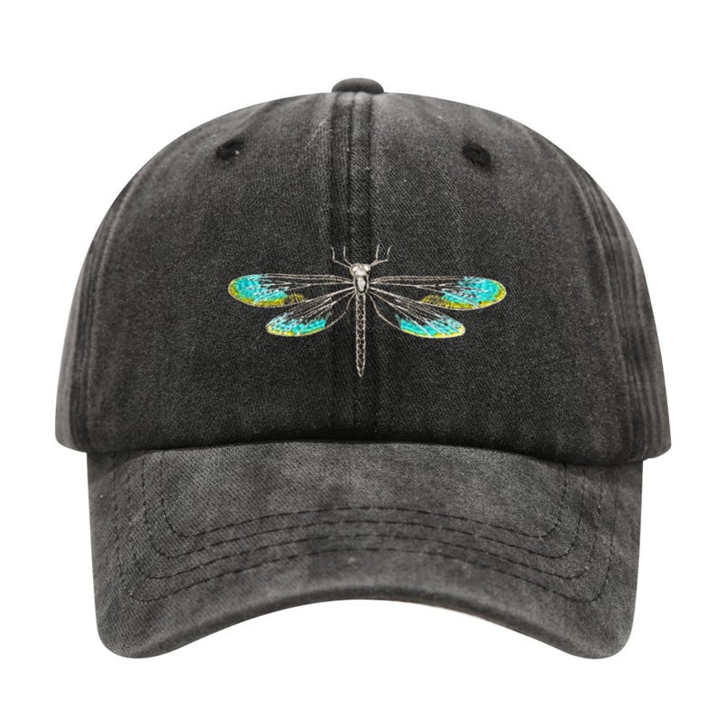 May include: A black baseball cap with a distressed finish. The cap features a detailed embroidered dragonfly design with teal and yellow wings. The cap has a curved brim and an adjustable strap.
