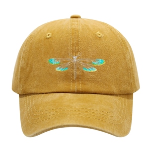May include: Mustard-colored baseball cap with a dragonfly embroidered on the front. The dragonfly has silver-colored body and turquoise and teal wings. The cap has a curved brim and a button on top.