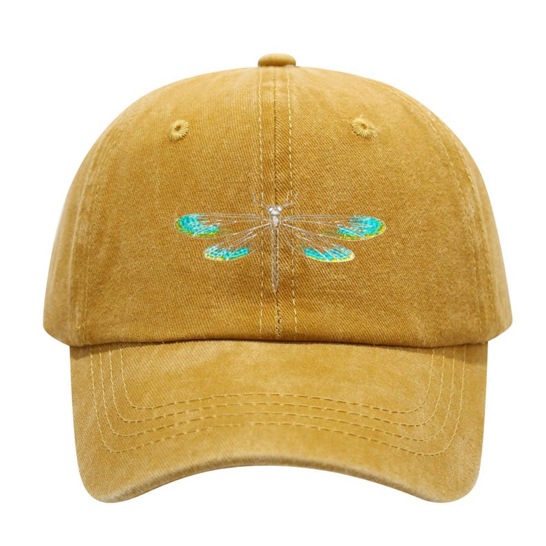 May include: Mustard-colored baseball cap with a dragonfly embroidered on the front. The dragonfly has silver-colored body and turquoise and teal wings. The cap has a curved brim and a button on top.