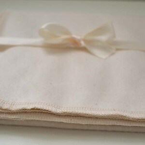 May include: A folded white cotton muslin cloth with a white satin ribbon tied in a bow.