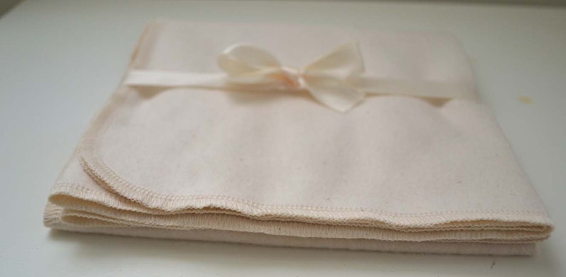 May include: A folded white cotton muslin cloth with a white satin ribbon tied in a bow.