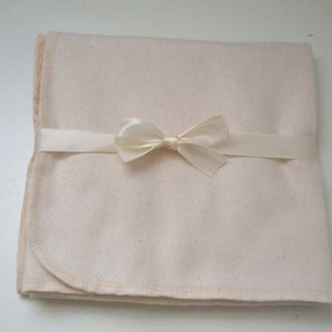 May include: A cream-colored, cotton baby blanket with a satin ribbon tied in a bow.