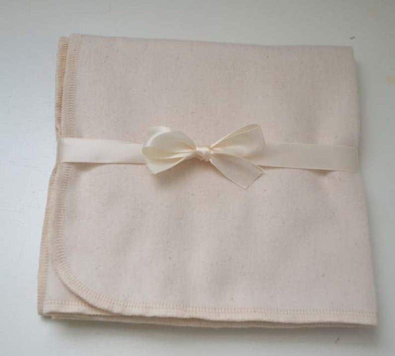 May include: A cream-colored, cotton baby blanket with a satin ribbon tied in a bow.