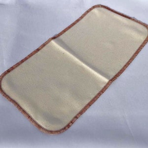 May include: A beige fabric insert with a brown stitched border. The insert is rectangular and has a smooth, even texture.