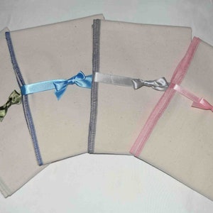 May include: Four white fabric squares with different colored ribbon bows. The ribbons are blue, silver, pink, and green.