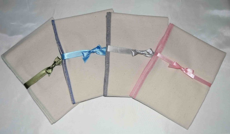 May include: Four white fabric squares with different colored ribbon bows. The ribbons are blue, silver, pink, and green.