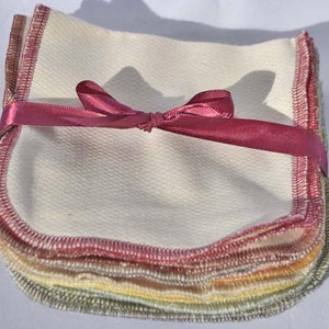 May include: A stack of 10 reusable cotton makeup remover pads with a pink ribbon tied around them. The pads are white with a light pink, yellow, and green trim around the edges.