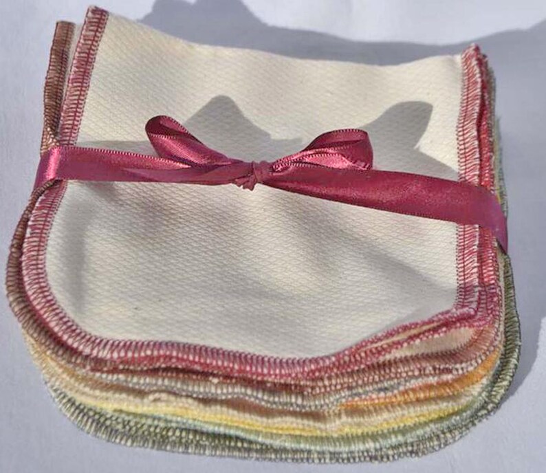 May include: A stack of 10 reusable cotton makeup remover pads with a pink ribbon tied around them. The pads are white with a light pink, yellow, and green trim around the edges.