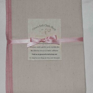 May include: A beige cloth square with pink edging, tied with a pink ribbon. The cloth is packaged with a white card that reads "Gina's Soft Cloth Shop" and includes care instructions and contact information.