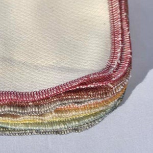May include: A stack of white cotton cloths with red, orange, yellow, green, and blue stitched edges.