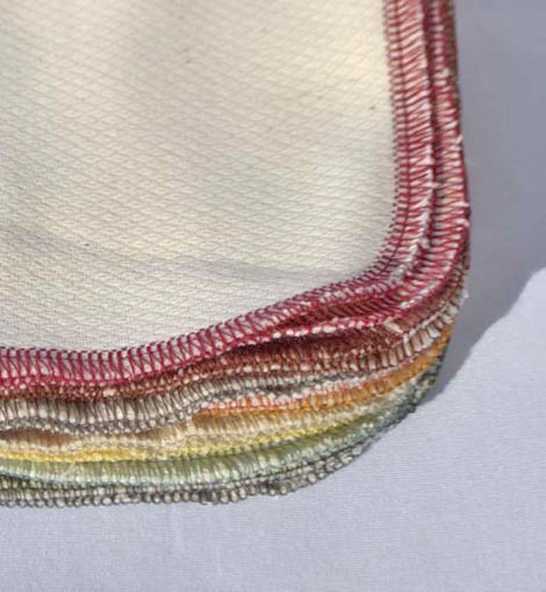 May include: A stack of white cotton cloths with red, orange, yellow, green, and blue stitched edges.