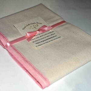 May include: A folded white cloth with pink trim, tied with a pink ribbon and a pink bow. A small card with the text "Gina's Soft Cloth Shop" is attached to the ribbon. The card includes washing instructions: "Machine wash, gentle cycle, tumble dry. No chlorine bleach or fabric softener. Find us at ginasoftclothshop.net. Or stop by our shop on Etsy and Amazon."