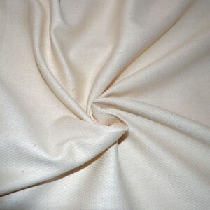 May include: Close-up of a white, textured fabric with a soft, smooth feel. The fabric is folded and draped, showcasing its natural texture and subtle sheen.