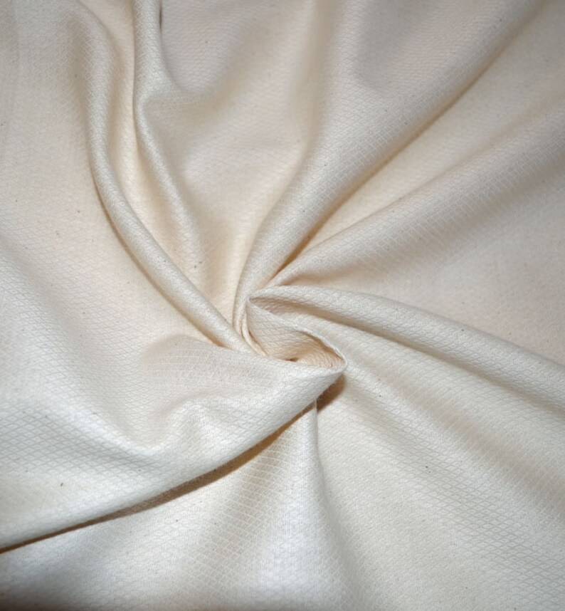 May include: Close-up of a white, textured fabric with a soft, smooth feel. The fabric is folded and draped, showcasing its natural texture and subtle sheen.