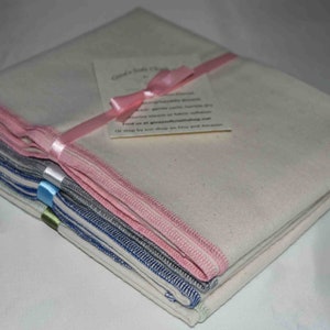 May include: A stack of white baby cloth burp cloths with pink, blue, and gray trim. The cloths are tied together with a pink ribbon and a small tag that reads "Cloth Baby Burp Cloths" and includes care instructions.