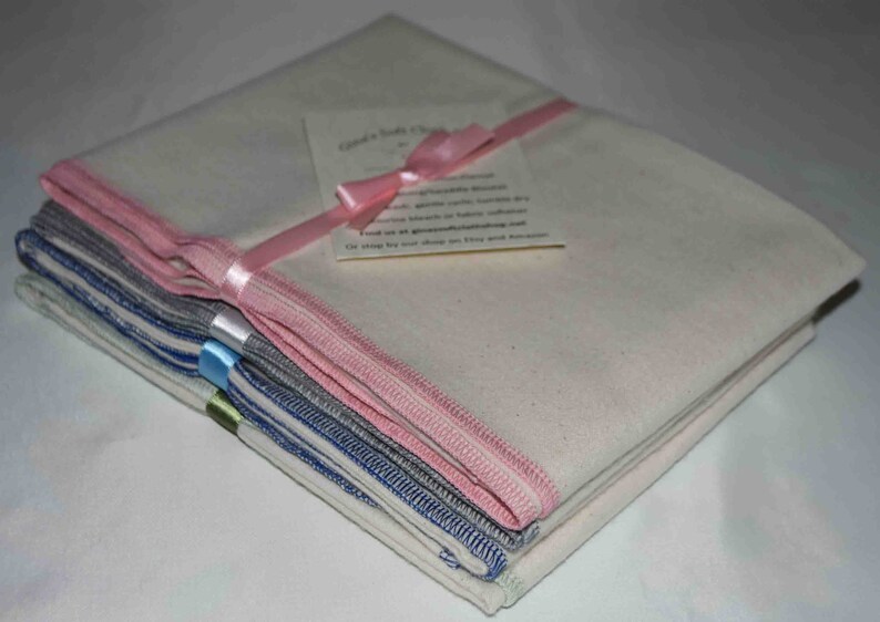 May include: A stack of white baby cloth burp cloths with pink, blue, and gray trim. The cloths are tied together with a pink ribbon and a small tag that reads "Cloth Baby Burp Cloths" and includes care instructions.