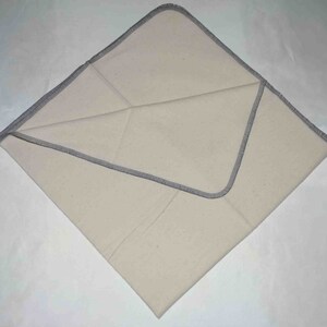 May include: A white cotton cloth with a gray stitched border. The cloth is folded in half and the edges are visible.