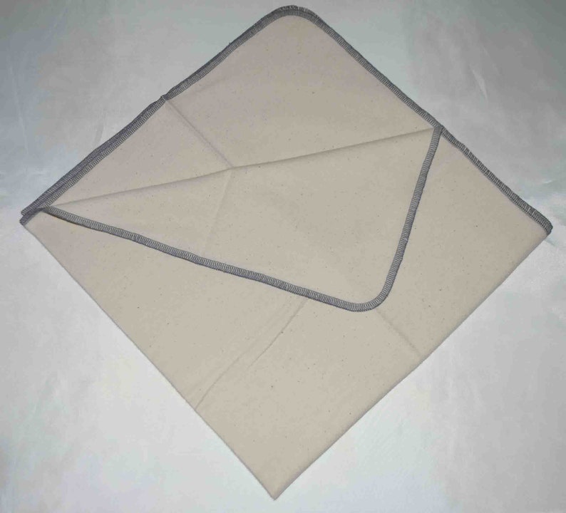 May include: A white cotton cloth with a gray stitched border. The cloth is folded in half and the edges are visible.