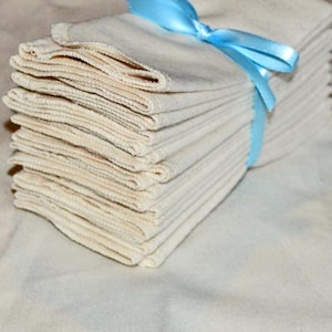 Può includere: Un mucchio di 15 panni di mussola di cotone bianco legati insieme con un nastro blu chiaro. I panni sono piegati a metà e impilati ordinatamente.