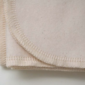 May include: Close-up of a folded piece of off-white fabric with a stitched edge. The fabric is soft and has a slightly textured surface.