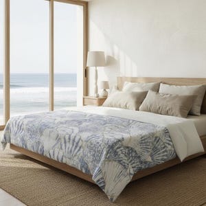 May include: A bed with a wooden frame and a blue and white seashell patterned comforter. The bed is made up with several pillows in neutral tones. A large window overlooks the ocean.