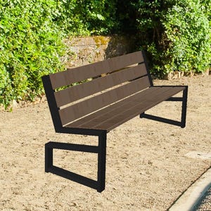 May include: A brown wooden park bench with a black metal frame sits on a sandy path. The bench is in a park setting, with green hedges and a curved walkway with a decorative railing. A pond with green water is visible.