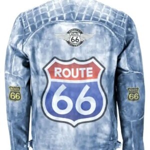 Puede incluir: Una chaqueta vaquera azul con un gran cartel de la Ruta 66 en la espalda. La chaqueta tiene un diseño acolchado y una cremallera. Hay parches más pequeños de la Ruta 66 en las mangas.
