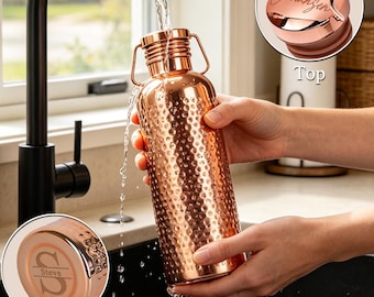Peut inclure: Une bouteille d'eau en cuivre martelé avec une poignée en métal et un bouchon à vis. Le couvercle supérieur porte le nom gravé Johansen, tandis que la base inférieure affiche la lettre S et le nom Steve. L'eau coule d'un robinet.