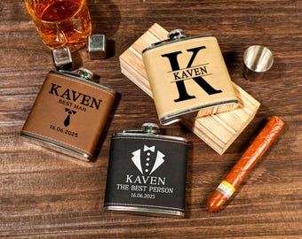 May include: An overhead shot features three personalized flasks with the name "Kaven" and dates. One is brown with "Best Man", another tan with a large "K", and the third black with a tuxedo graphic. A glass of amber liquid, ice cubes, a shot glass, and a cigar are also present.