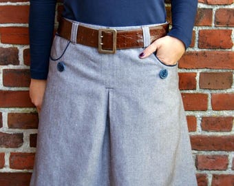 May include: A gray skirt with a brown leather belt and blue buttons. The skirt has a pleated front and a slightly flared hem.
