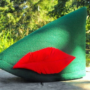 May include: A green felt hat with a red felt feather attached to the front. The hat is pointed and has a wide brim.