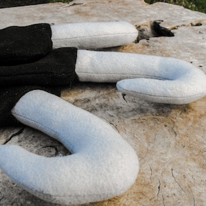 May include: Three felt, curved objects in the shape of a candy cane. The main body is black, with a white, curved end. The objects are lying on a weathered, light brown surface.