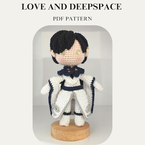 Peut inclure: Poupée Zayne au crochet de Love and Deepspace, avec des cheveux noirs et une tenue blanche et marine. La poupée est présentée sur une base en bois. Le texte sur l'image indique "Zayne (Master of Fate) Love and Deepspace PDF Pattern."