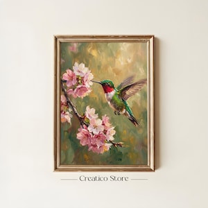 May include: A framed painting of a hummingbird hovering near pink cherry blossoms. The bird has green, red, and white feathers. The painting has a gold frame and the text "Creatico Store" at the bottom.