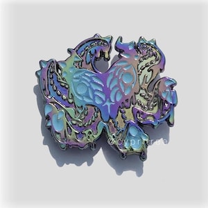 Puede incluir: Pin esmaltado iridiscente con un diseño de criatura estilizada con detalles intrincados. El pin tiene un efecto de cambio de color, mostrando tonos de azul, morado y verde. El diseño incluye una figura central con formas de garra y una superficie texturizada.