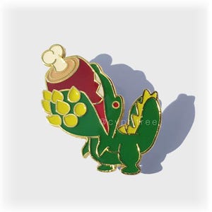 May include: A green and yellow enamel pin of a cartoon dinosaur eating a red and white drumstick.