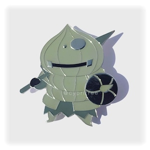 May include: A light green enamel pin depicting a cartoon character with a bulbous head, holding a sword and shield. The character has a smiling mouth and a circular eye. The pin is set against a white background.