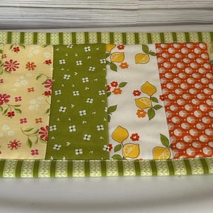 May include: A green and yellow patchwork table runner with a variety of floral and geometric patterns.